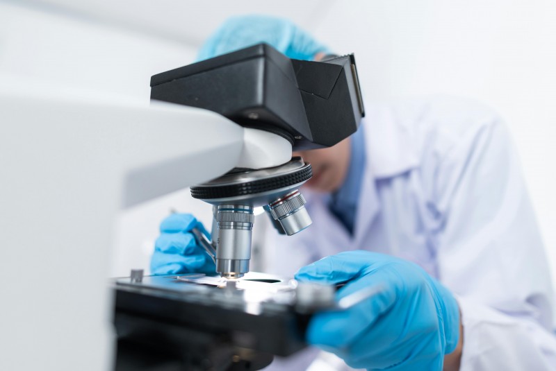 persona borrosa con ropa de laboratorio mirando tras microscopio
