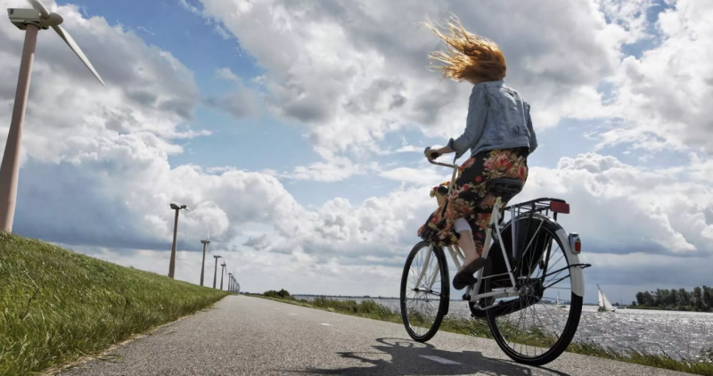 Chica andando en bici junto a un canal a la derecha y molinos de viento a la izquierda