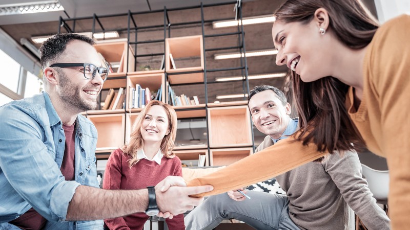 Hombre y mujer estrechándose la mano mientras otras dos personas miran, todos sonríen